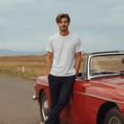 Mann trägt weißes BREDDY’S TENCEL™ T-Shirt und blaue BREDDY’S Pants vor rotem Cabrio
