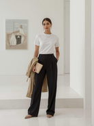 Frau in moderner Galerie trägt weißes BREDDY’S TENCEL™ T-Shirt und schwarze BREDDY’S Pants