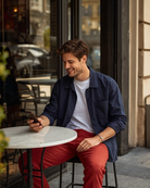 Mann sitzt im Café, trägt rote BREDDY’S Pants mit weißem TENCEL™ T-Shirt und schaut auf sein Handy