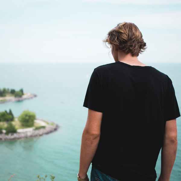 Mann trägt schwarzes BREDDY’S TENCEL™ T-Shirt und schaut aufs Wasser mit Insel in der Mitte